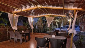 An outdoor patio with tables and chairs, covered by a wooden roof with hanging fans. - O'NEST Countryside (Murud)