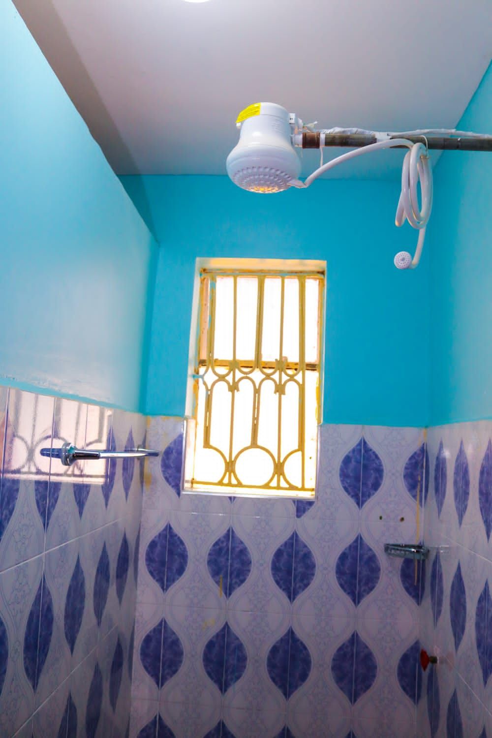 Un baño con ducha, una ventana con barrotes y azulejos estampados.