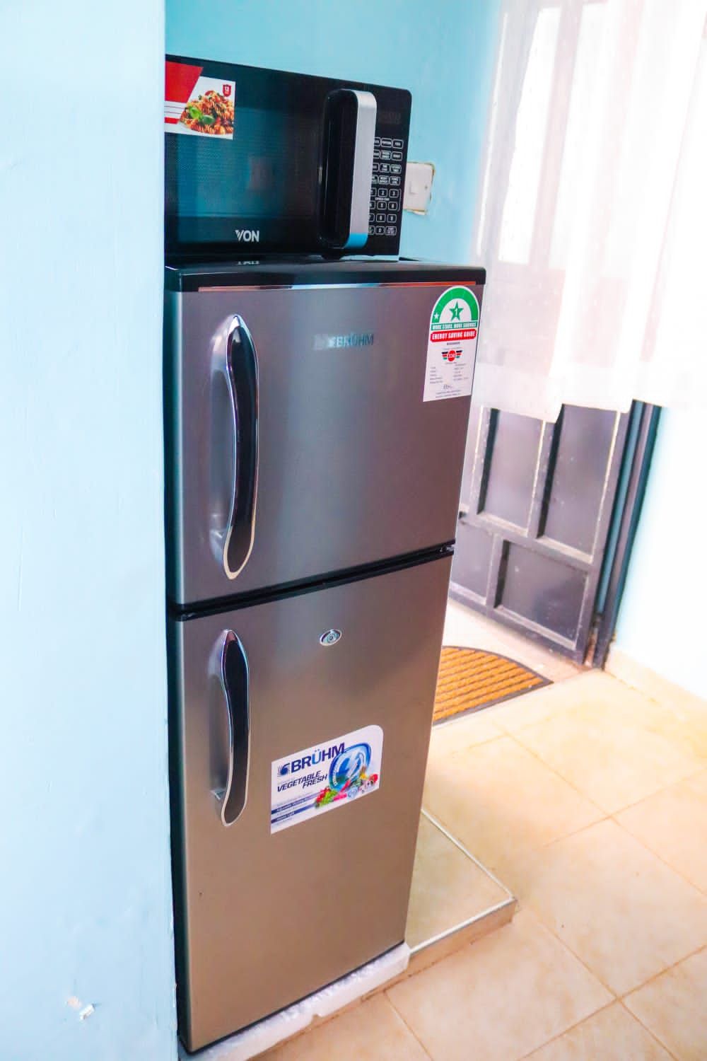 Un refrigerador de acero inoxidable con un microondas encima, dos puertas y calcomanías que indican que es un congelador para vegetales.
