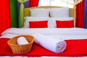 A neatly made bed with white and red bedding, a rolled white towel, and a wicker basket with a rolled white towel. - Milimani Suites Kisumu (Kisumu)