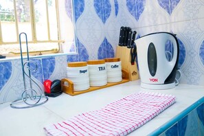 A kitchen counter with a kettle, jars labeled 'Sugar', 'Tea', and 'Coffee', a knife block, and a red and white striped cloth. - Milimani Suites Kisumu (Kisumu)