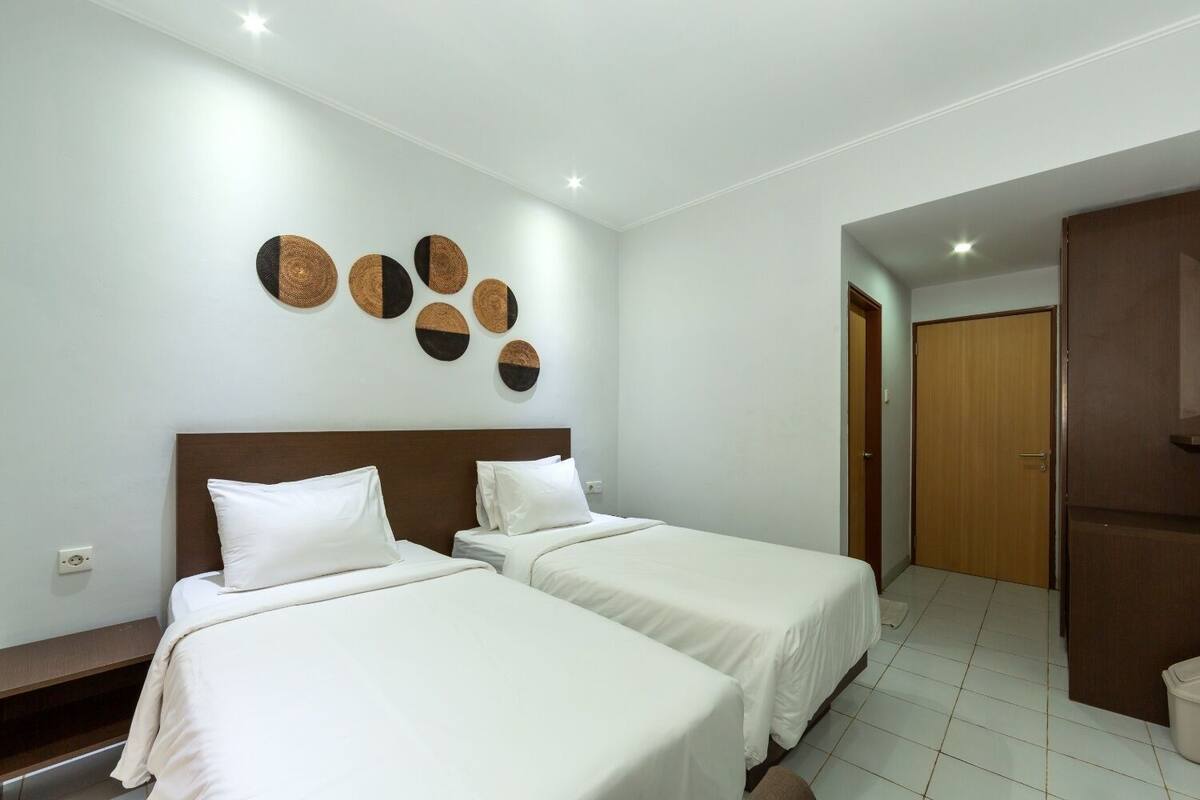 A hotel room with two beds, a wooden headboard, a wall with circular wall art, and a wooden door.