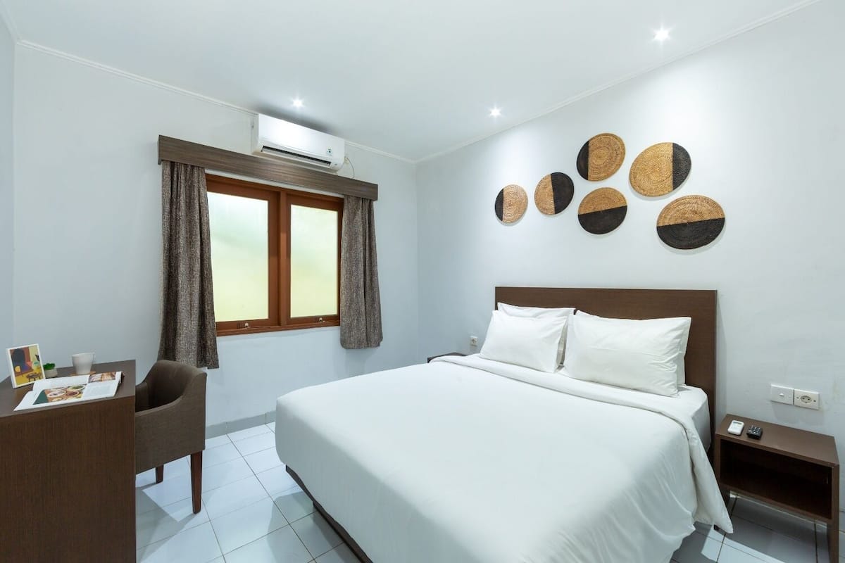 A hotel room with a large bed, a desk with a chair, a window with curtains, and wall art.