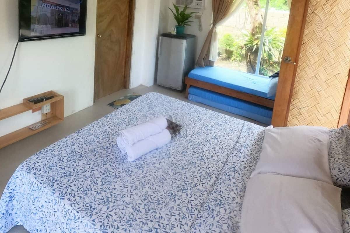 A bedroom with a bed, a TV mounted on the wall, a small table, and a window with curtains.