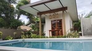 A swimming pool with a covered area, surrounded by greenery and a concrete wall. - Marelocca Beach House  (Calatagan)
