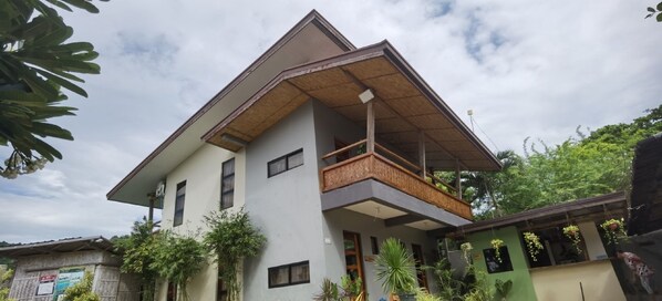 A two-story house with a balcony, surrounded by greenery and a clear sky. - Marelocca Beach House (Calatagan)