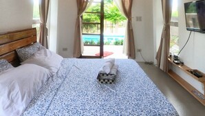 A bedroom with a bed, curtains, a TV, and a view of a pool. - Marelocca Beach House  (Calatagan)