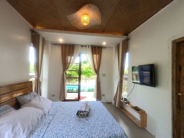 Un dormitorio con cama, cortinas, televisión y vista a una piscina.