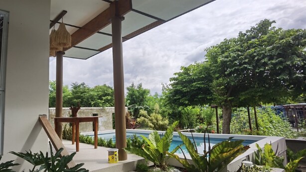 A covered outdoor area with a pool, wooden furniture, and lush greenery. - Marelocca Beach House  (Calatagan)