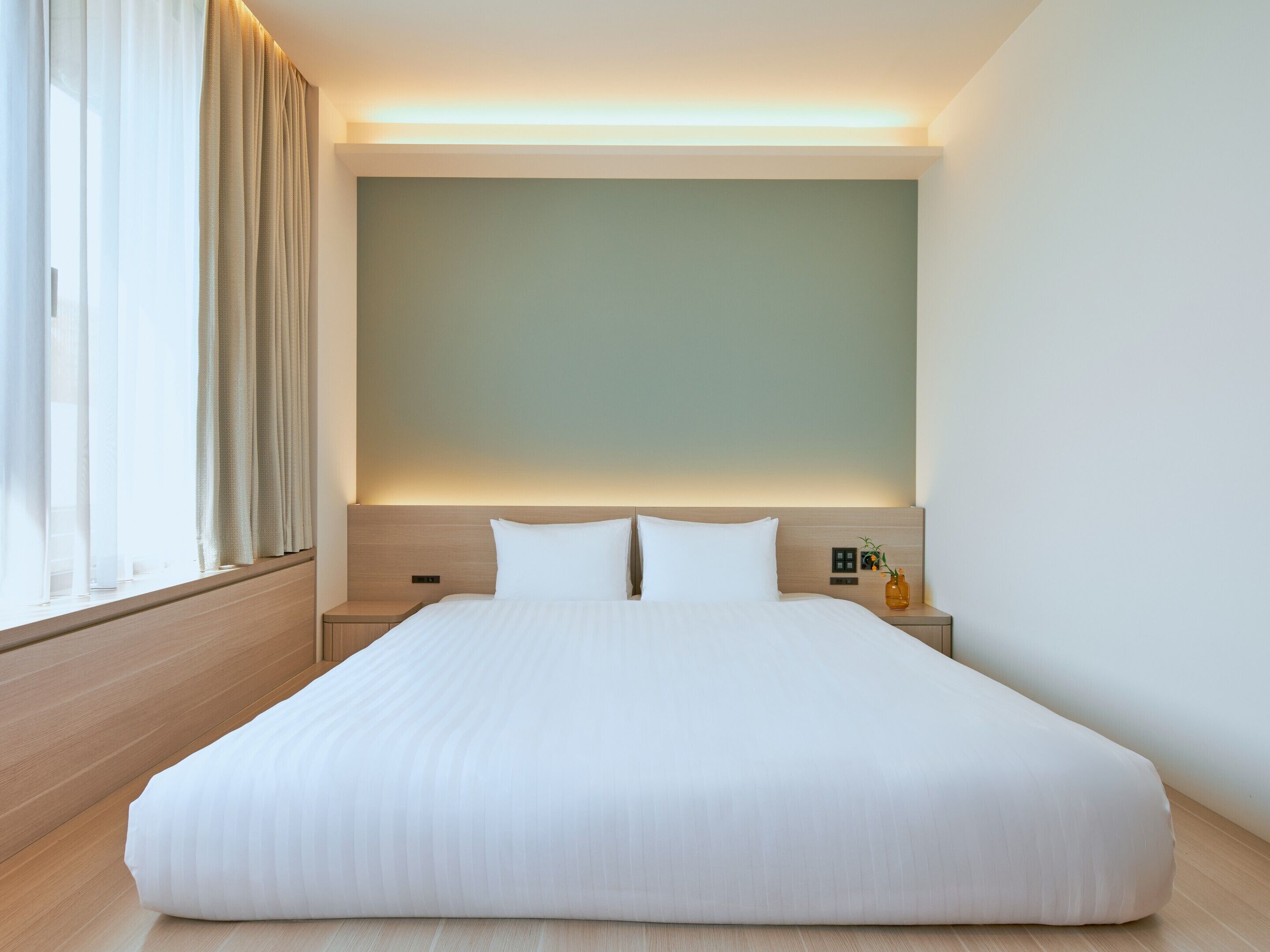 Une chambre d’hôtel avec un grand lit, une table de chevet, un panneau de commande fixé au mur et une fenêtre avec des rideaux.