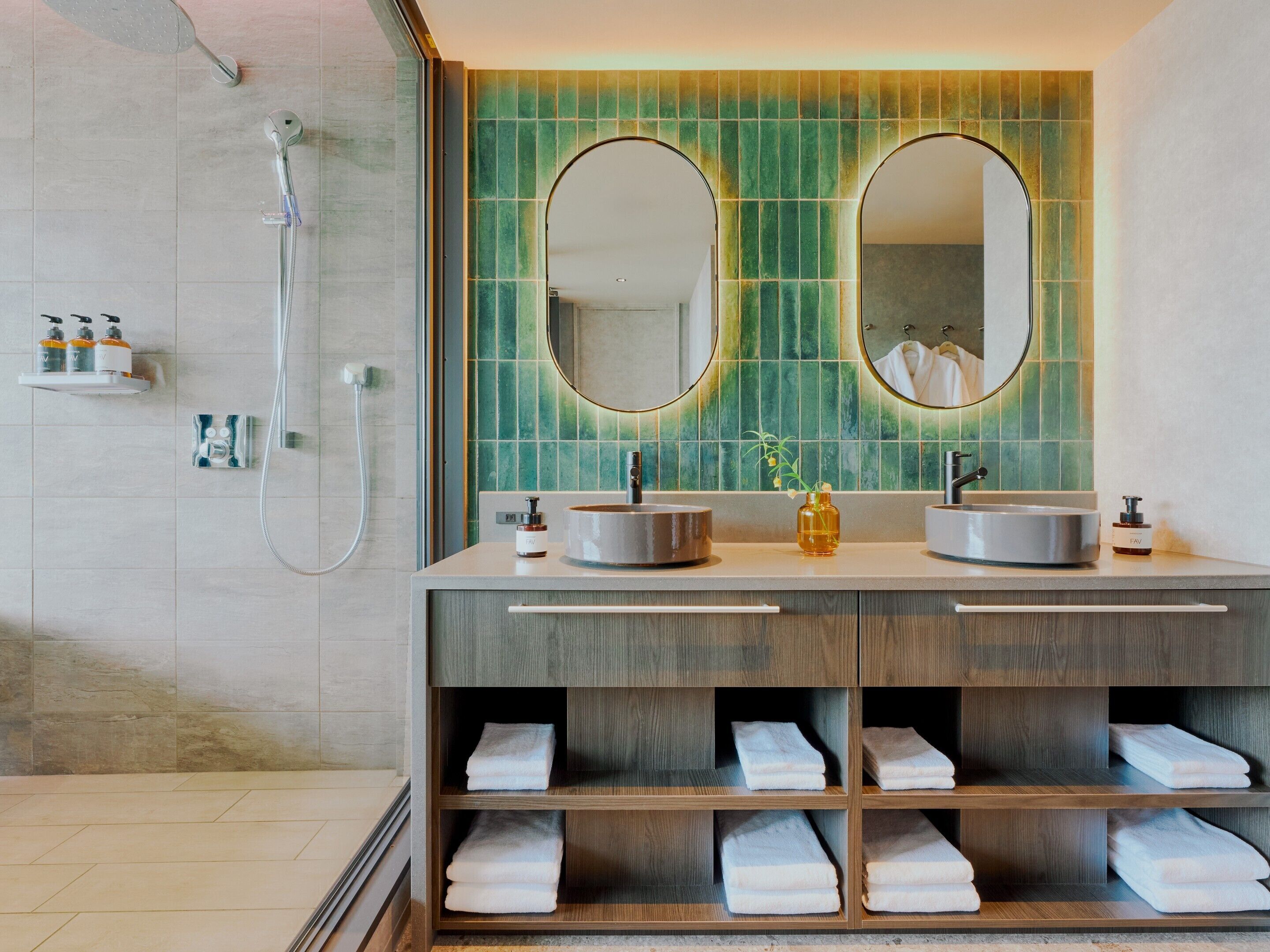 A modern bathroom with dual sinks, a shower, and a vanity with shelves for towels.