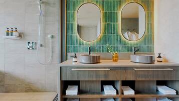 A modern bathroom with dual sinks, a shower, and a vanity with shelves for towels.
