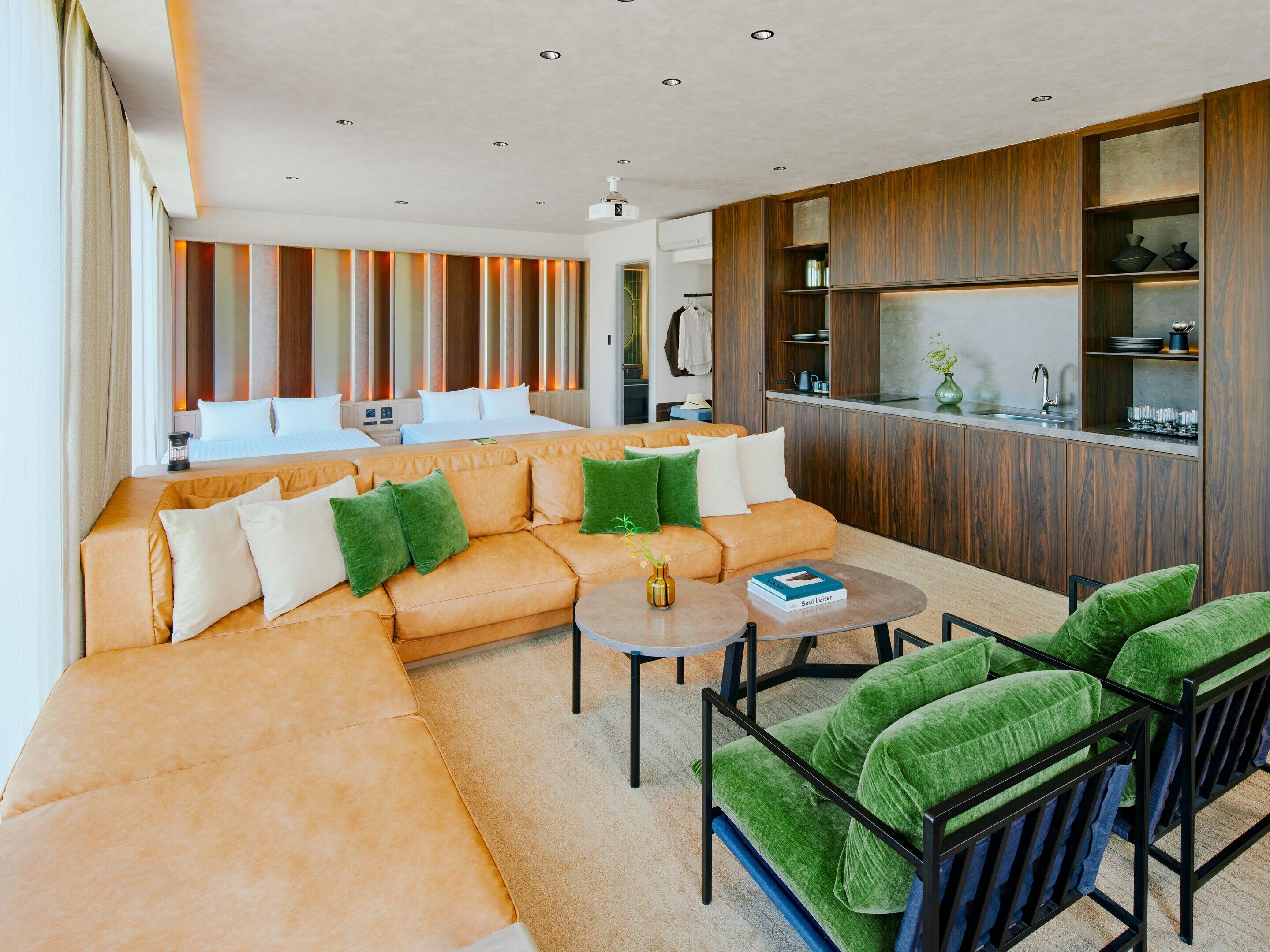 A modern living room with a sofa, green cushions, a coffee table, and a kitchen area with wooden cabinets.