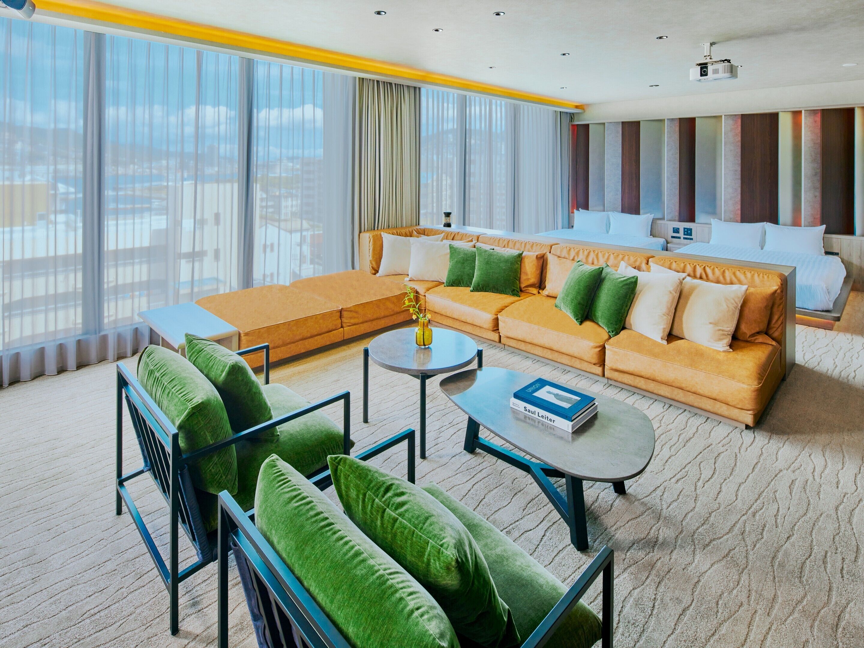 Una habitación de hotel moderna con un sofá grande, un sofá más pequeño, una mesa de centro y una cama.