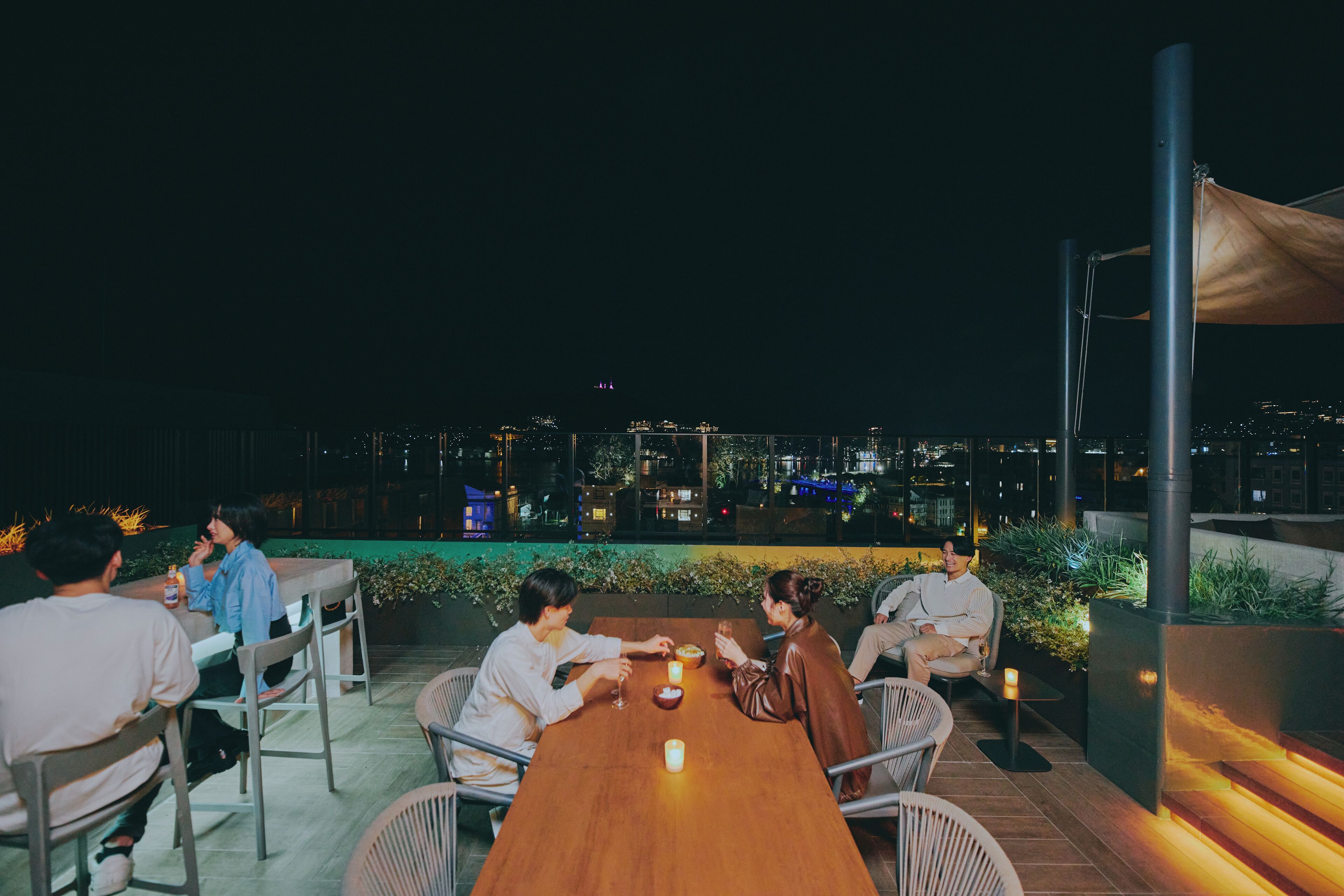 A group of people dining at an outdoor table with a city view at night.