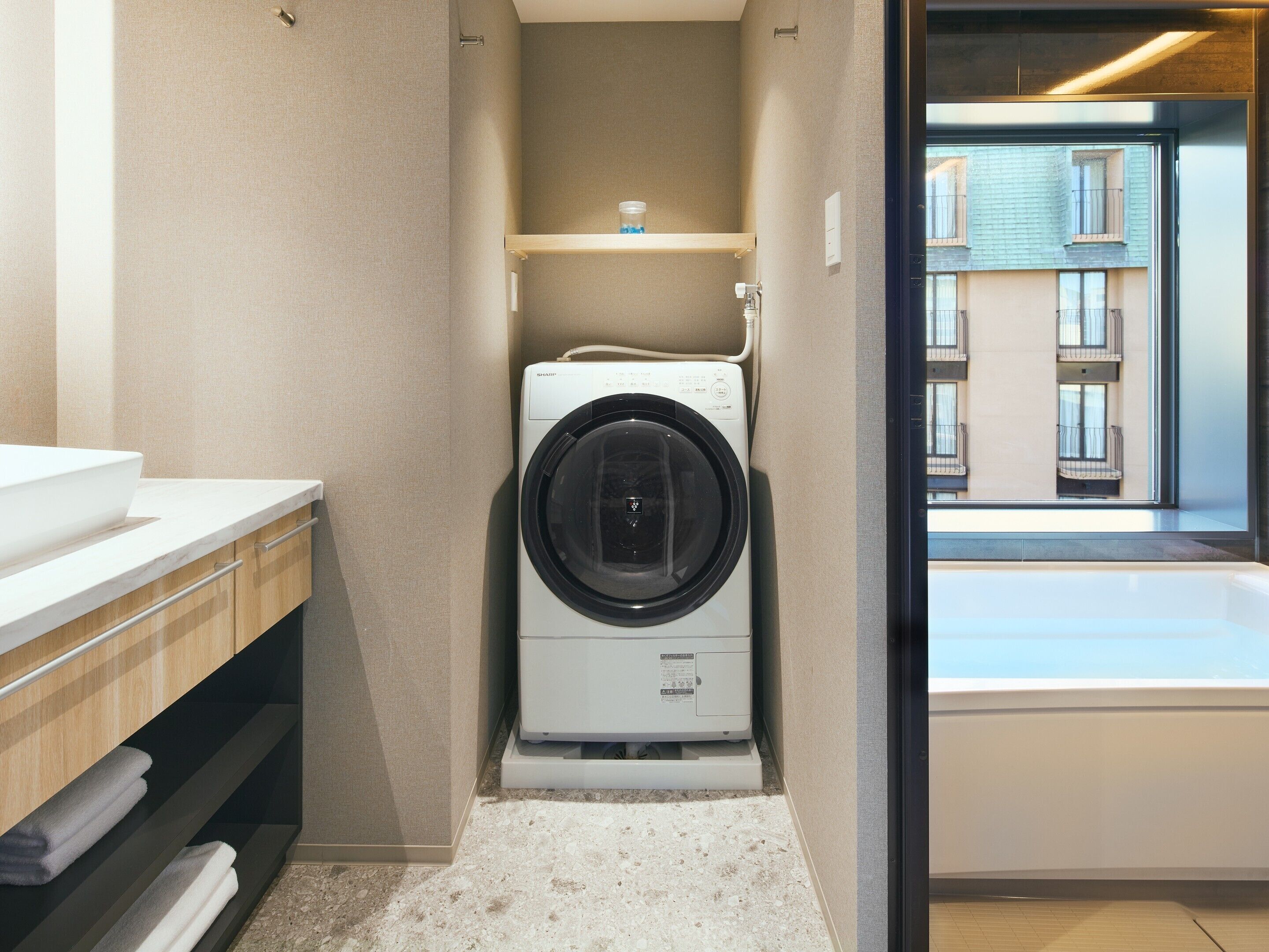 A compact laundry room with a washing machine, a sink, and a view of a building through a window.