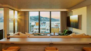 A modern hotel room with a large window, a flat-screen TV, a wooden bar area, and a city view.