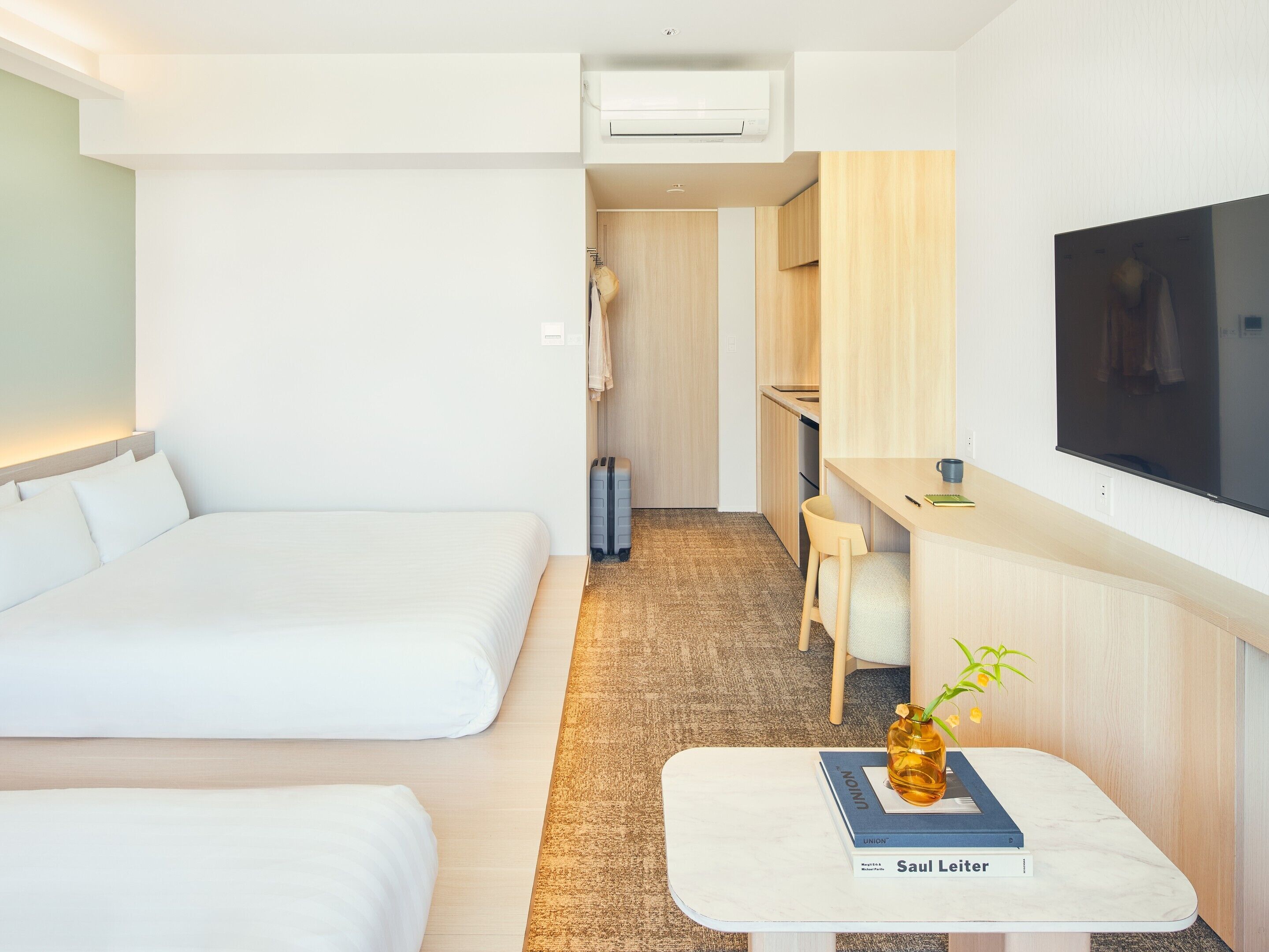 Habitación de hotel con cama, escritorio, televisión y una pequeña mesa con un libro y un jarrón.