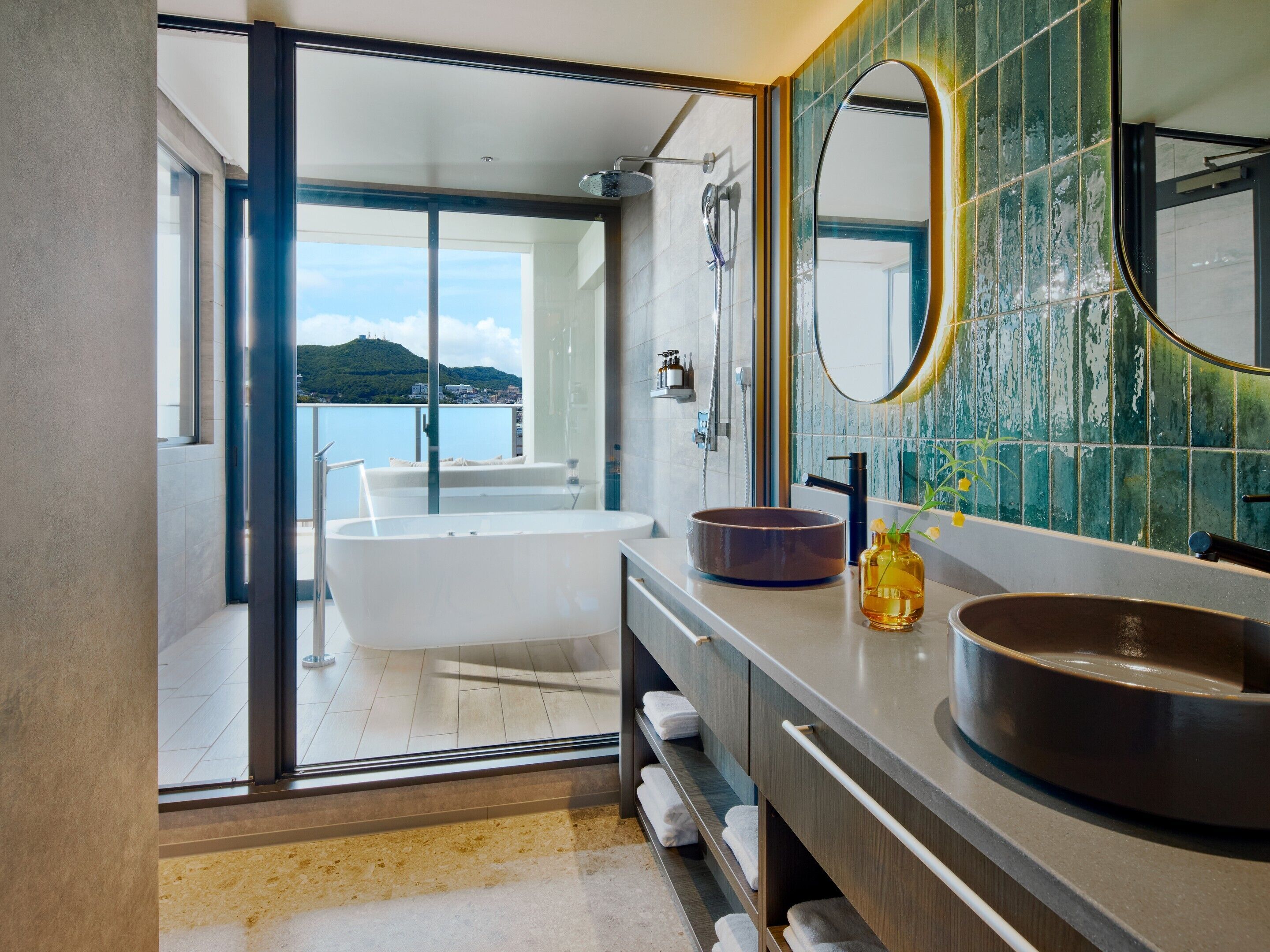 A modern bathroom with a bathtub, a large mirror, and a view of a body of water.
