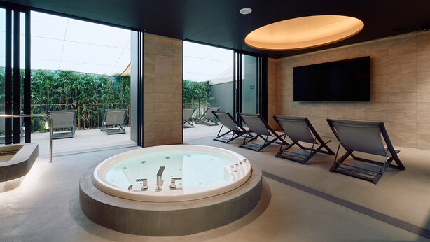 A modern spa area with a hot tub, reclining chairs, a flat-screen TV, and a view of greenery through large windows. - FAV LUX NAGASAKI (Nagasaki)