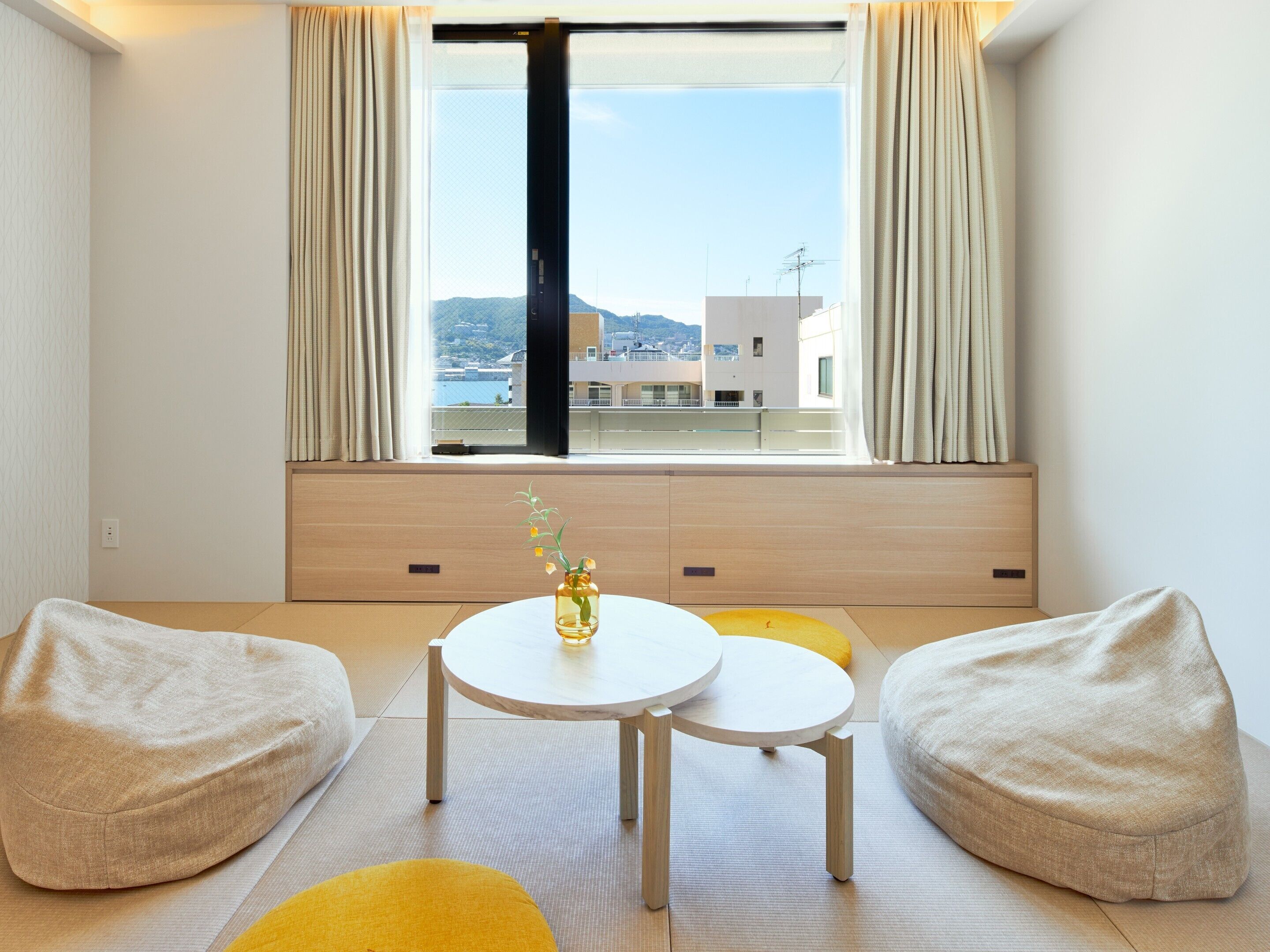 A modern room with a large window, two bean bag chairs, a small round table, and a vase with flowers.