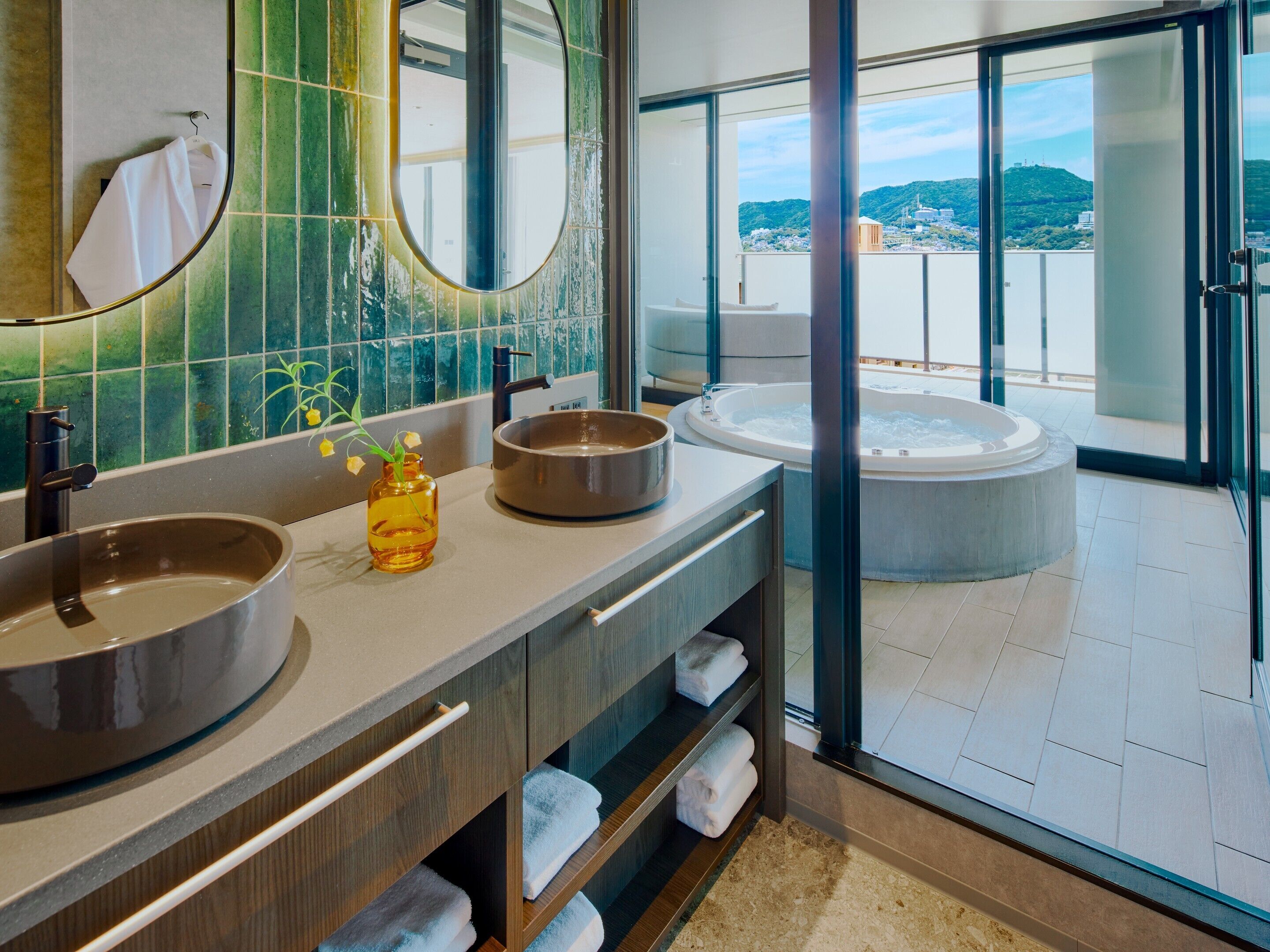 A modern bathroom with two sinks, a large mirror, and a view of a hot tub and cityscape.