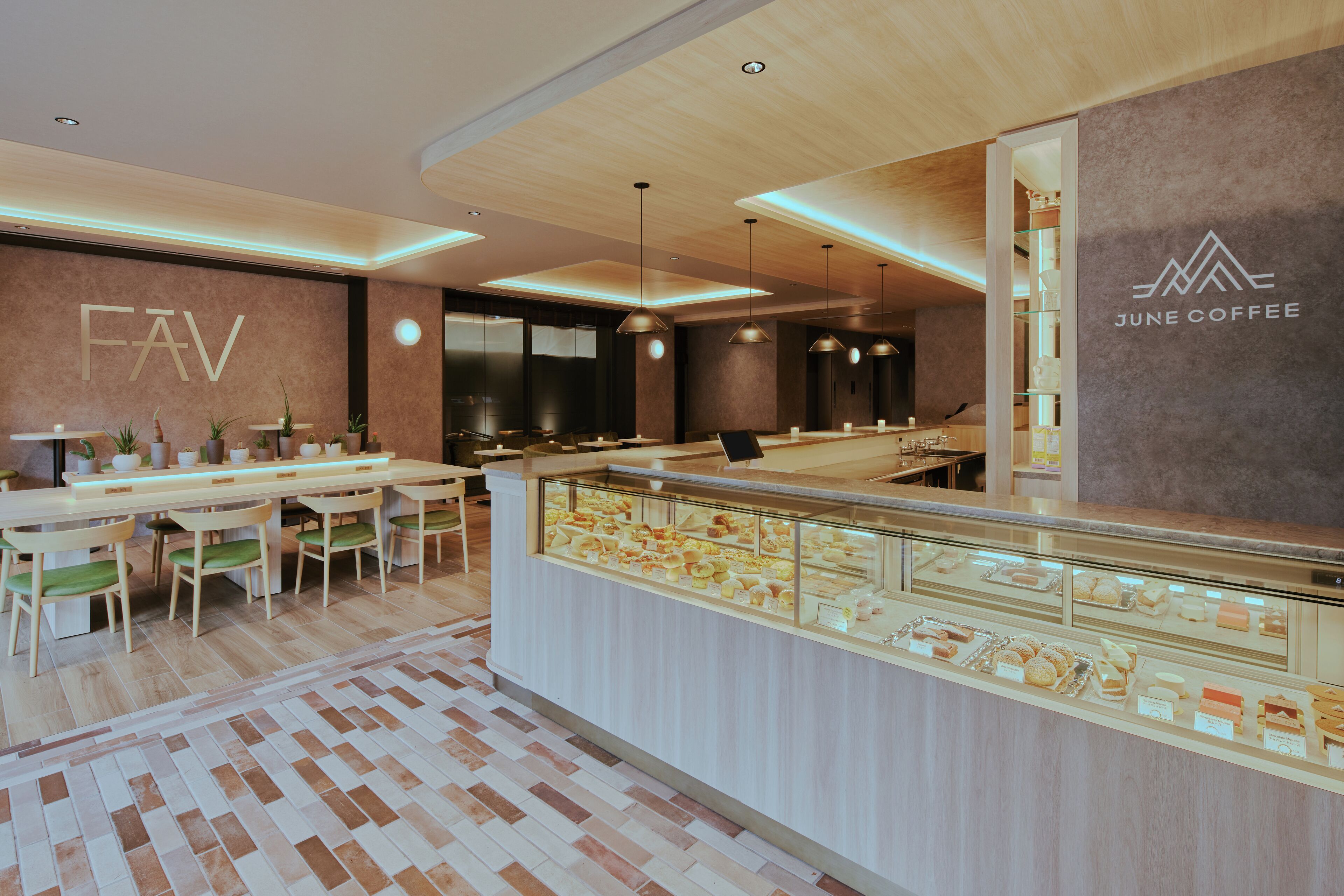 A modern cafe interior with a wooden ceiling, a glass display case of pastries, and a seating area with wooden tables and chairs.