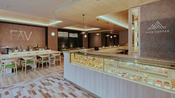 A modern cafe interior with a wooden ceiling, a glass display case of pastries, and a seating area with wooden tables and chairs.