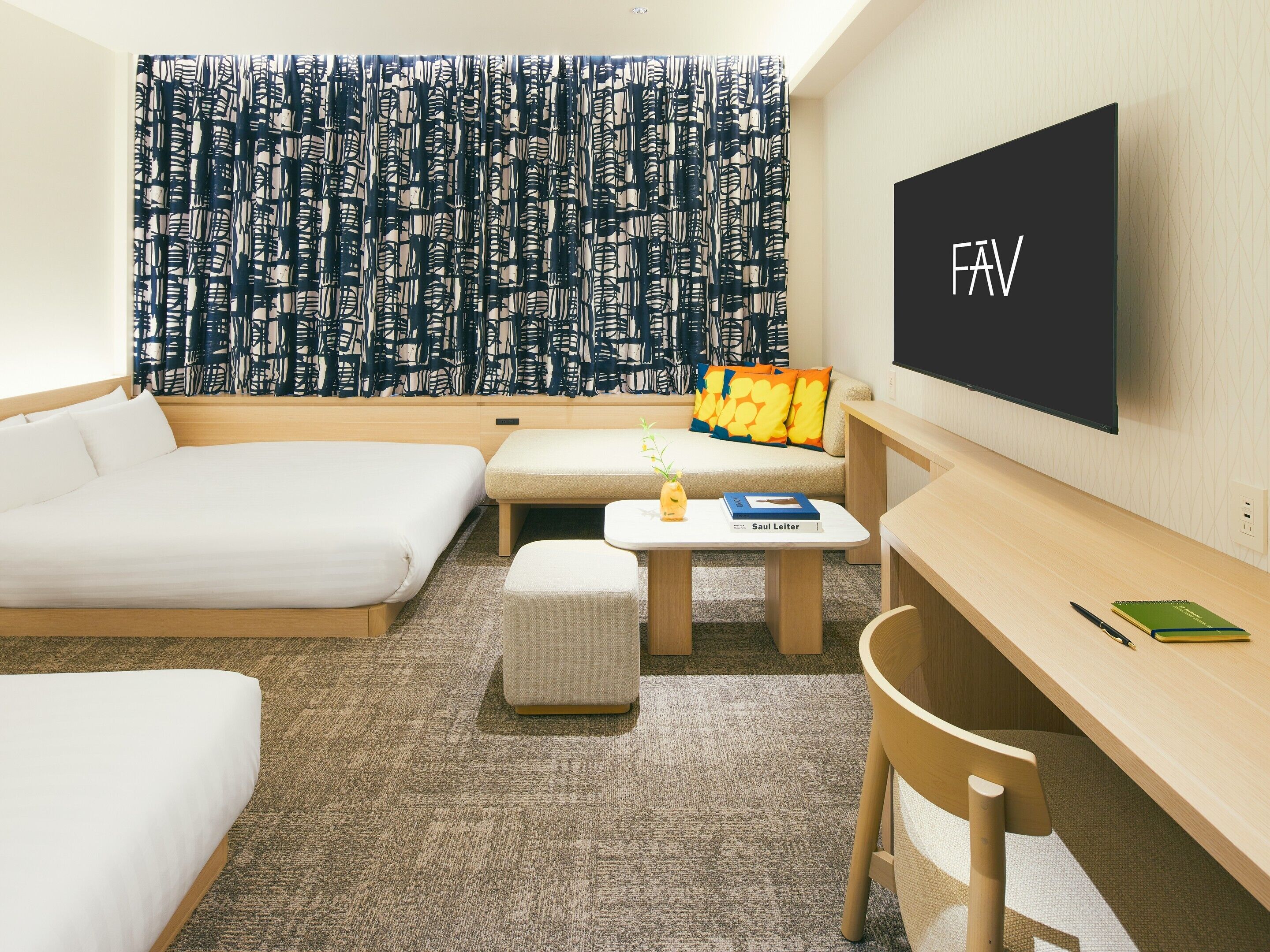 A modern hotel room with a sofa, a desk, a small table, and a TV mounted on the wall.