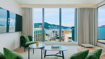A modern hotel room with a large window, a sofa, a small table, and a green chair.