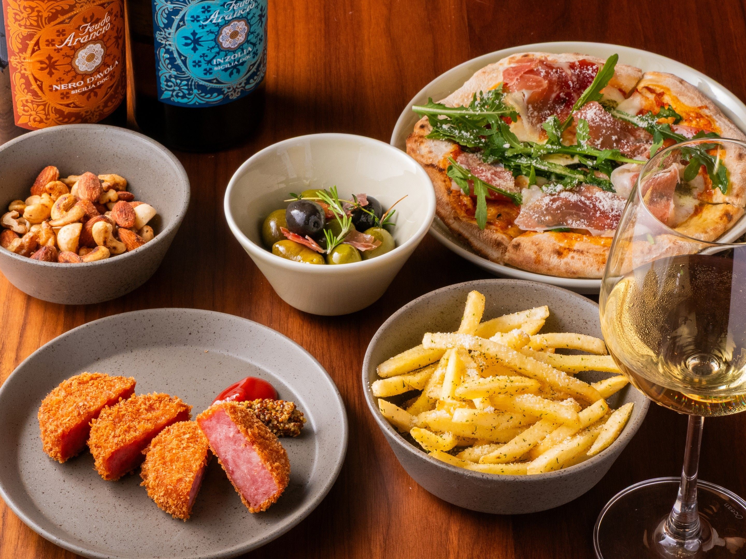 A table with various dishes including pizza, fries, and a bowl of olives.