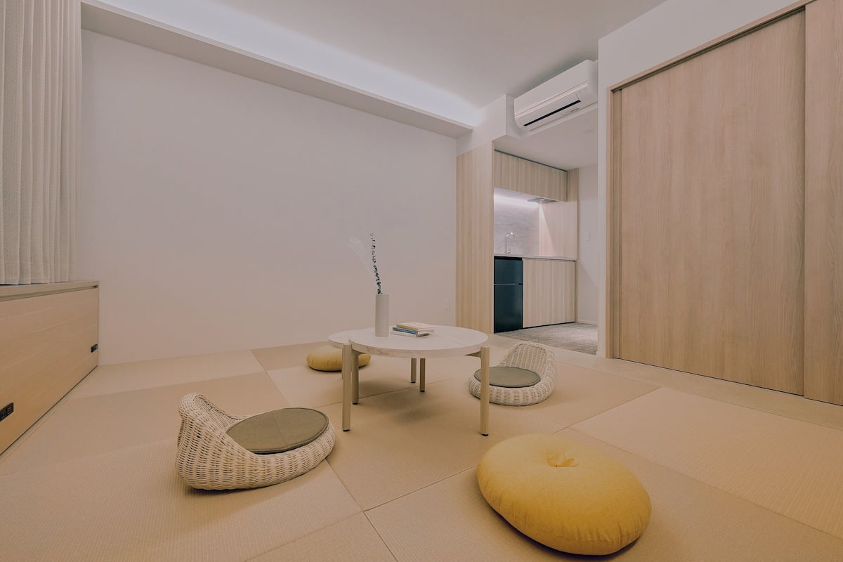 A minimalist room with a round table, two cushions, a small rug, and a wardrobe.