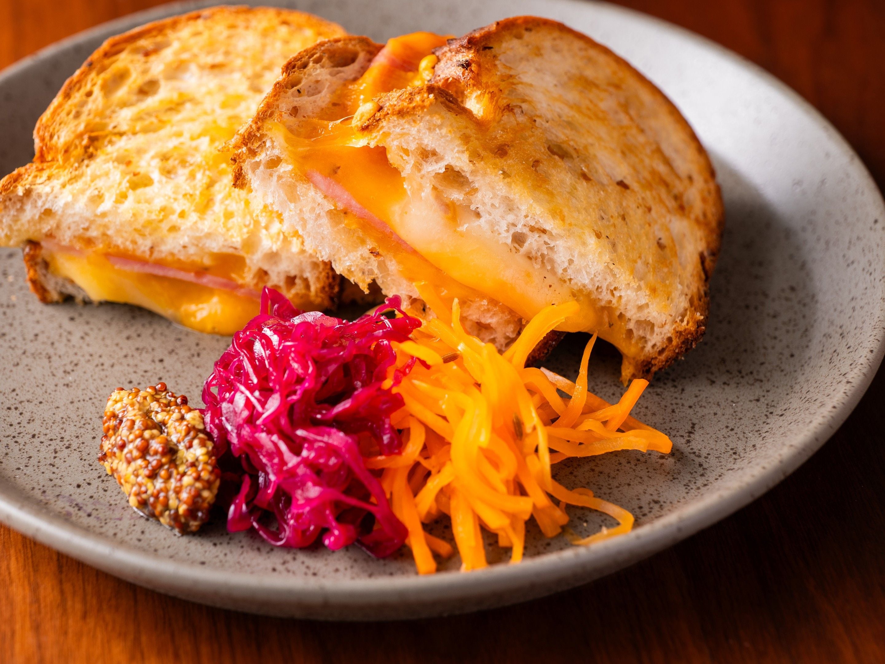 A sandwich with melted cheese and ham on a plate, accompanied by a side of shredded carrots and red cabbage.