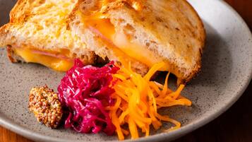 A sandwich with melted cheese and ham on a plate, accompanied by a side of shredded carrots and red cabbage.