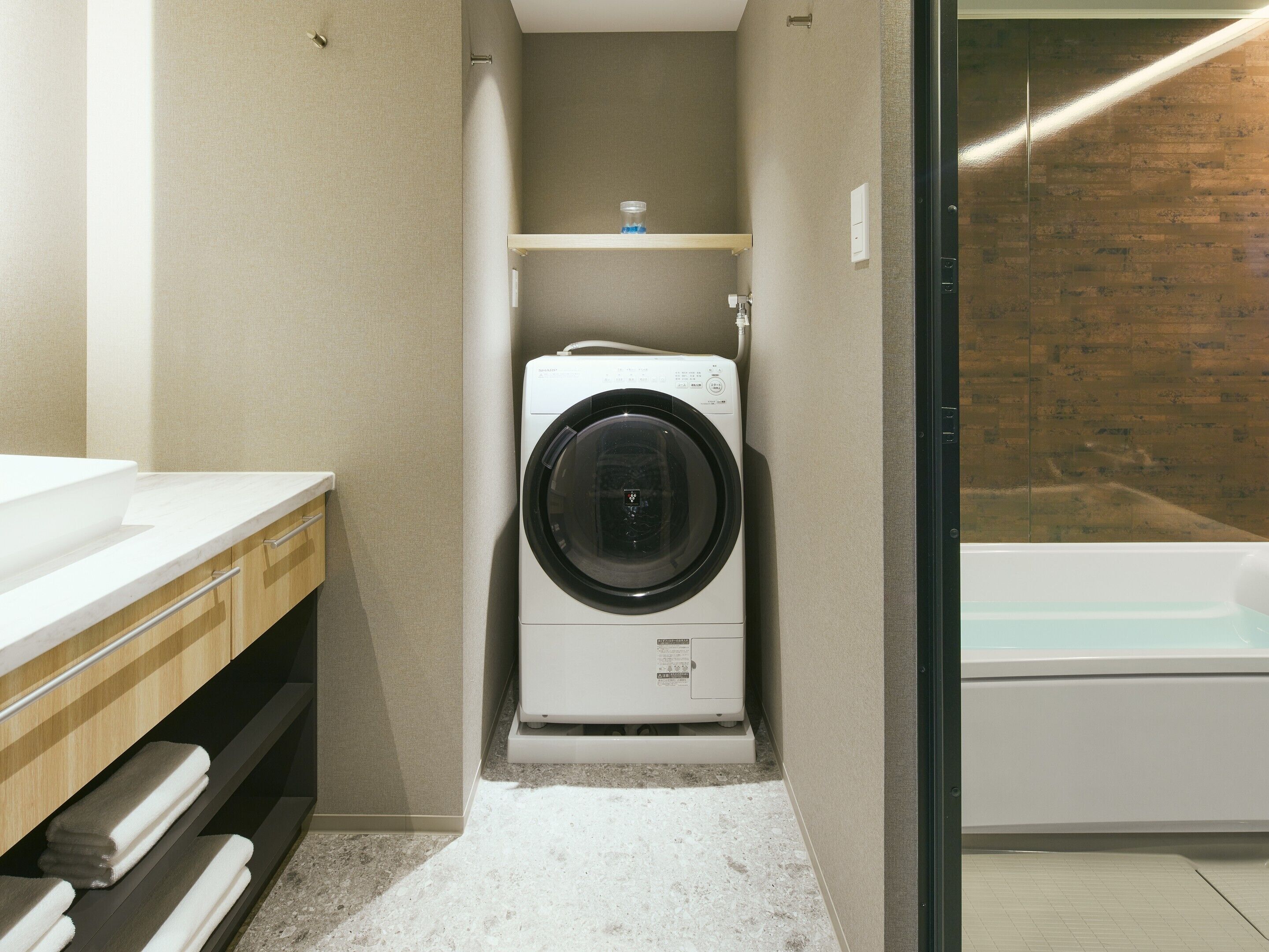 Une salle de bain compacte équipée d’un lave-linge et d’un sèche-linge intégrés, d’une petite étagère pour les articles de toilette et d’une baignoire.
