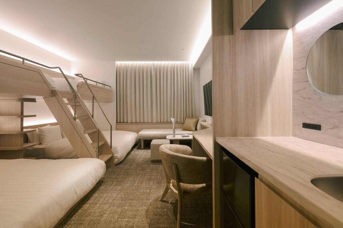 A modern hotel room with bunk beds, a desk, a chair, and a small seating area.