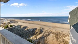 Une vue sur la plage depuis un balcon doté d’une balustrade, avec une plage de sable et l’océan en toile de fond.