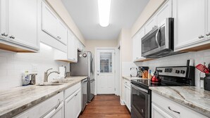 Une cuisine moderne avec des meubles blancs, des appareils en acier inoxydable et un plancher en bois.