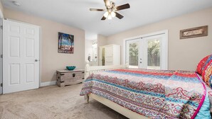Une chambre  à coucher avec un lit, un ventilateur de plafond, une commode, un miroir et une porte.