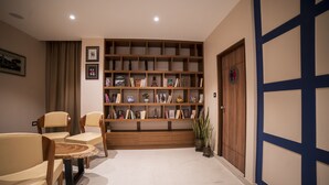 A room with a wooden bookshelf, two chairs, a small table, and a door with a blue frame. - Zip By Spree Hotels Gangtok (Gangtok)
