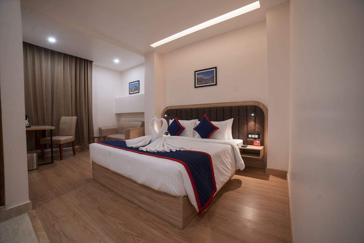 A hotel room with a large bed, a desk, a chair, and a nightstand.