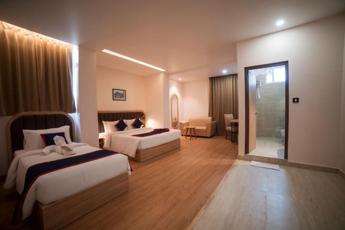 Une chambre d’hôtel avec deux lits, un coin salon et une salle de bain visible à travers une porte ouverte.