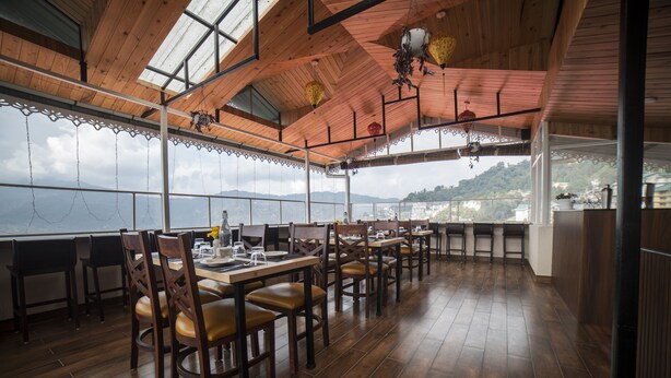 A restaurant with wooden tables and chairs, a high ceiling with hanging lanterns, and a view of the mountains. - Zip By Spree Hotels Gangtok (Gangtok)