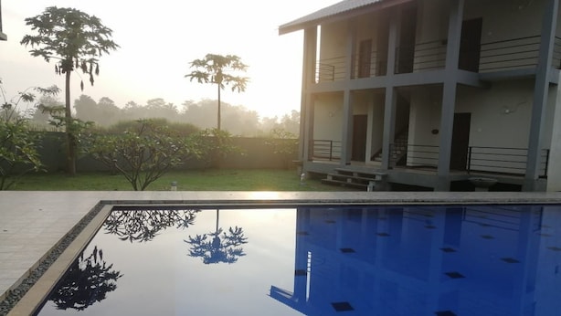 A swimming pool with a clear reflection of trees and a building in the background. - Sigiriya Retreats (Sigiriya)