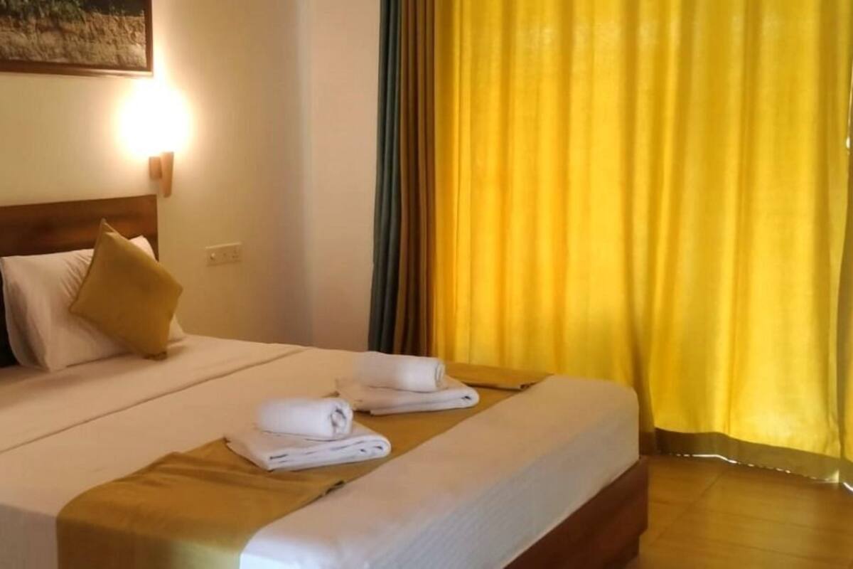 A neatly made bed with white linens and two gold pillows, a folded towel, and a wooden headboard.