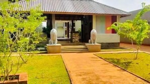 A building with a tiled roof, a front entrance, and a small garden area with two planters and a pathway. - Sigiriya Retreats (Sigiriya)