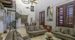 A spacious living room with a high ceiling, a spiral staircase, and a large window with wooden shutters. - Luxury Large Apartment With Colonial Balcony (Cartagena)