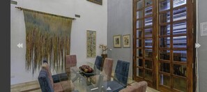 A dining area with a glass table, blue chairs, a fruit bowl, and a large woven tapestry. - Luxury Large Apartment With Colonial Balcony (Cartagena)