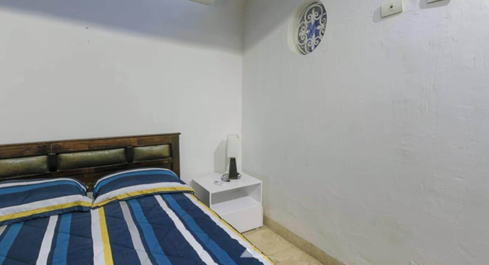 A bedroom with a bed, a nightstand, a wall socket, and a decorative plate.