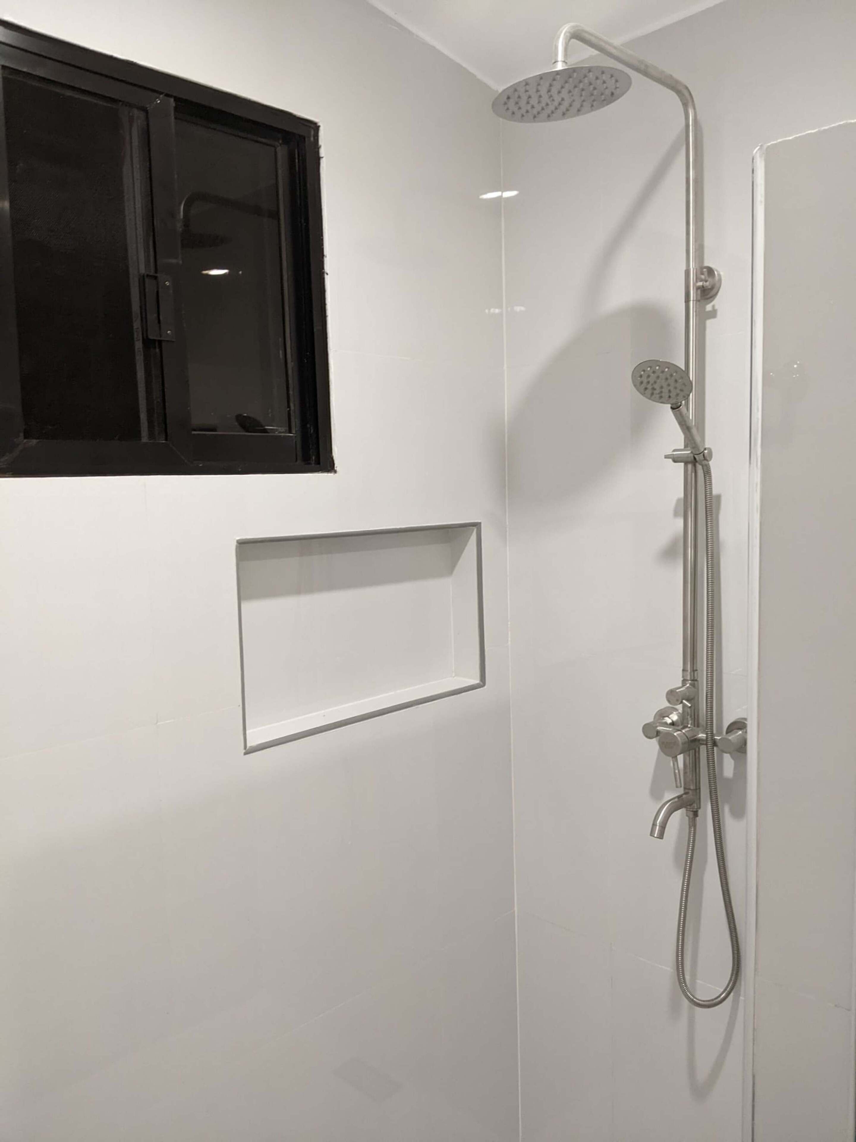 A modern bathroom with a shower, a window, and a built-in shelf.